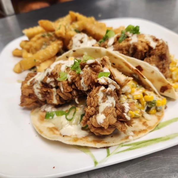 Crispy chicken tacos with corn salsa, drizzled with white sauce and served with french fries.