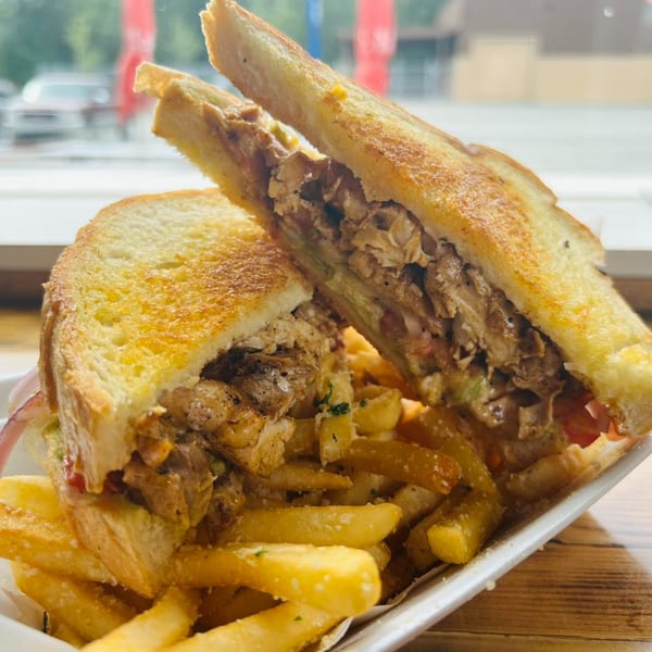 A grilled chicken sandwich with fries, served in a white basket on a wooden table.